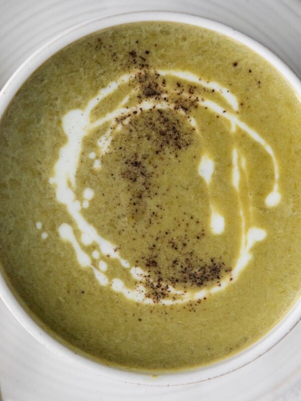 asparagus soup in a white bowl with a swirl of cream on top and a crack of pepper