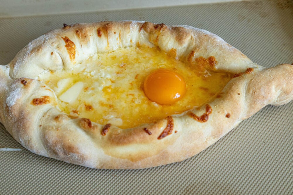 picture of baked khachapuri with egg on top on baking sheet