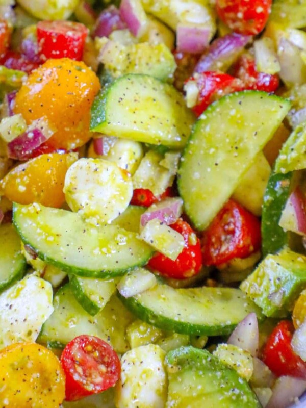 chopped cucumbers, cherry tomatoes, onion, crumbled feta cheese, and basil in a white bowl tossed in pesto sauce