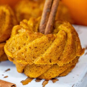 Moist spiced pumpkin bundt cakes with cinnamon sticks on a white plate.