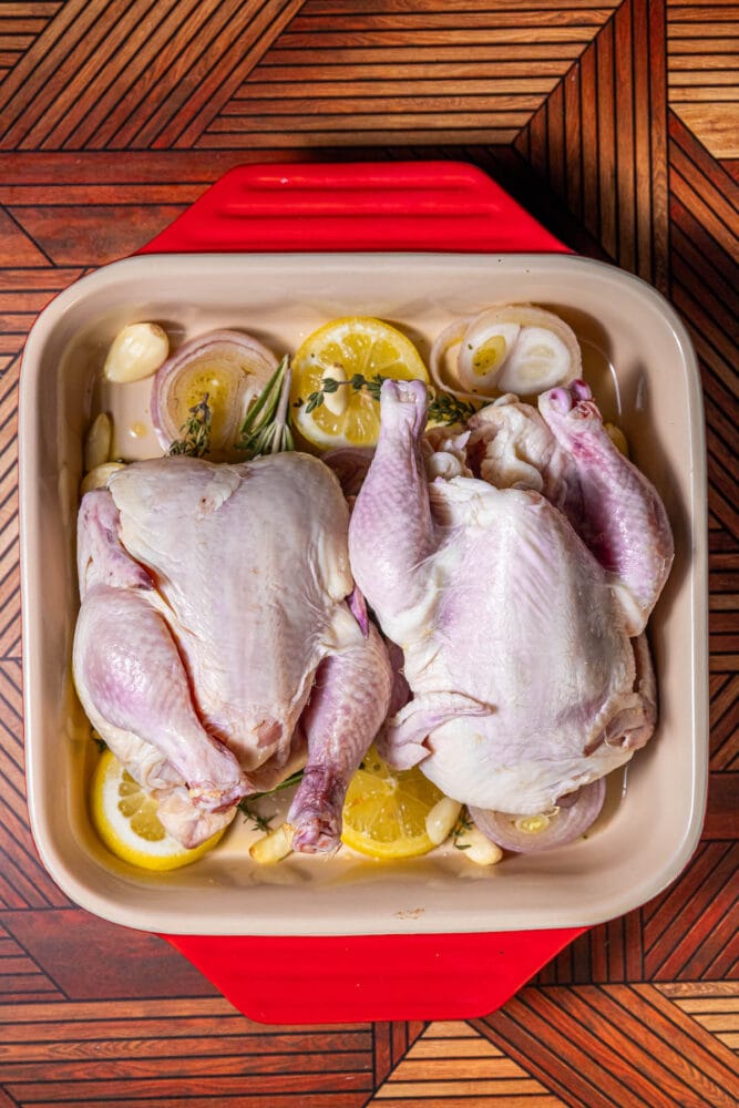 dry cornish game hens on top of lemon, shallot, and herbs in baking dish