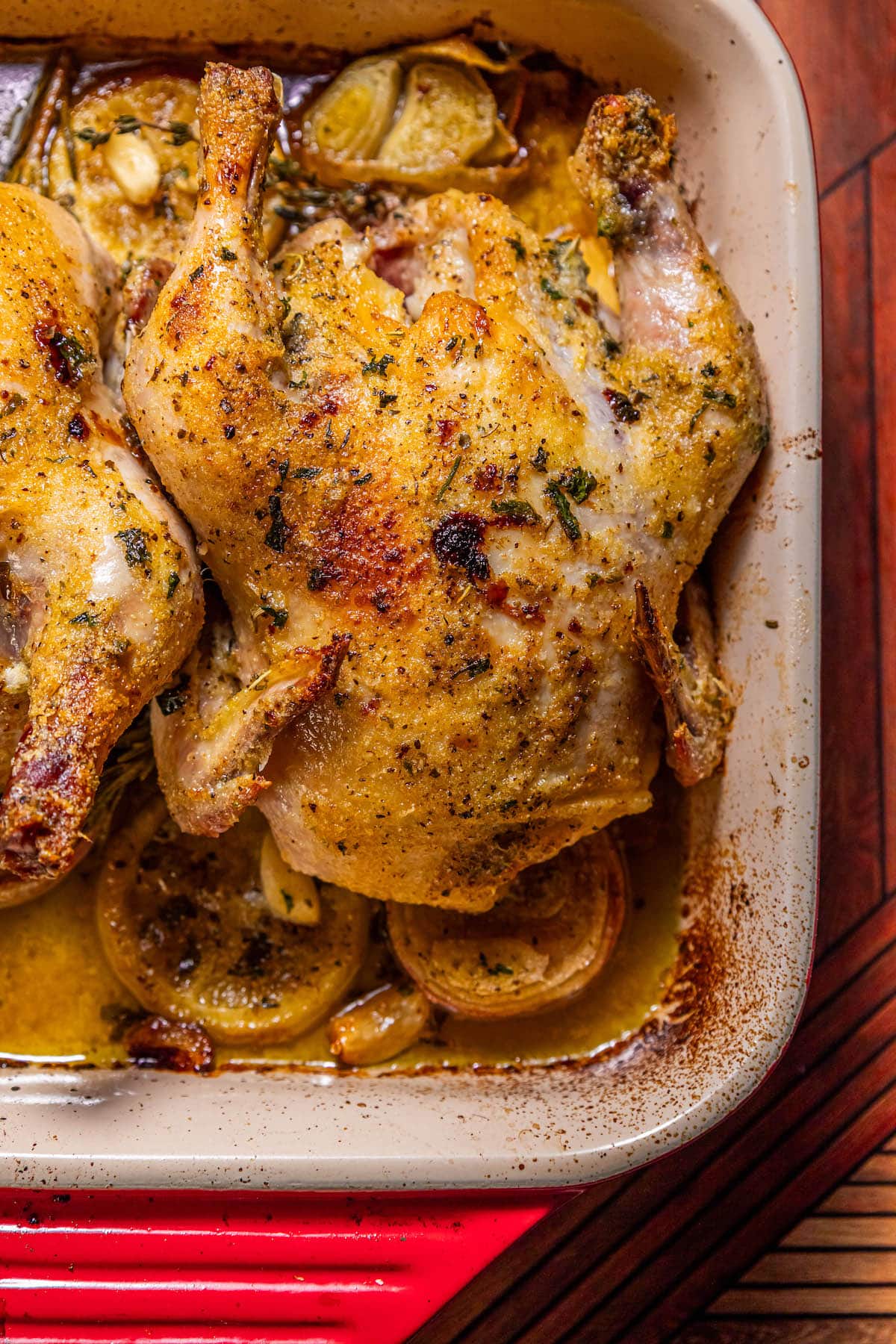 crispy roasted cornish game hen in a square baking dish with lemons, shallots, and garlic