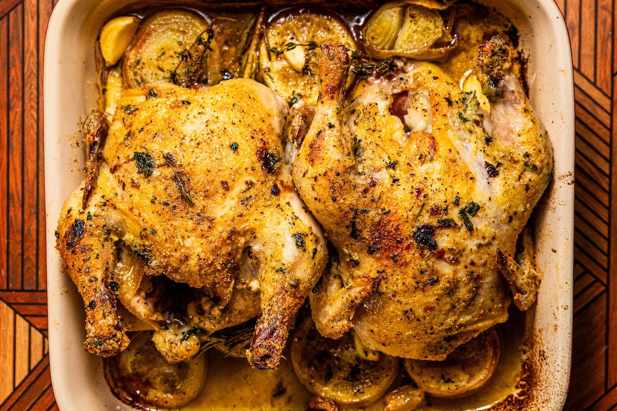 crispy roasted cornish game hen in a square baking dish with lemons, shallots, and garlic