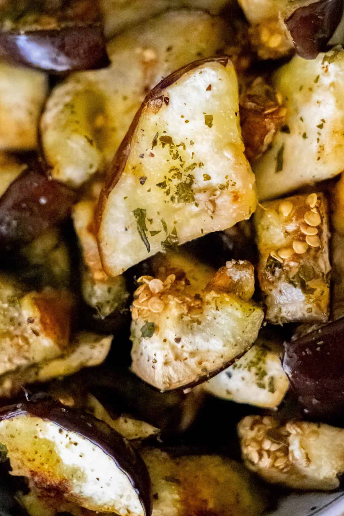 Close-up of roasted eggplant pieces seasoned with herbs and spices, showcasing golden-brown edges and visible seeds—a perfect highlight for delicious roasted eggplant recipes.