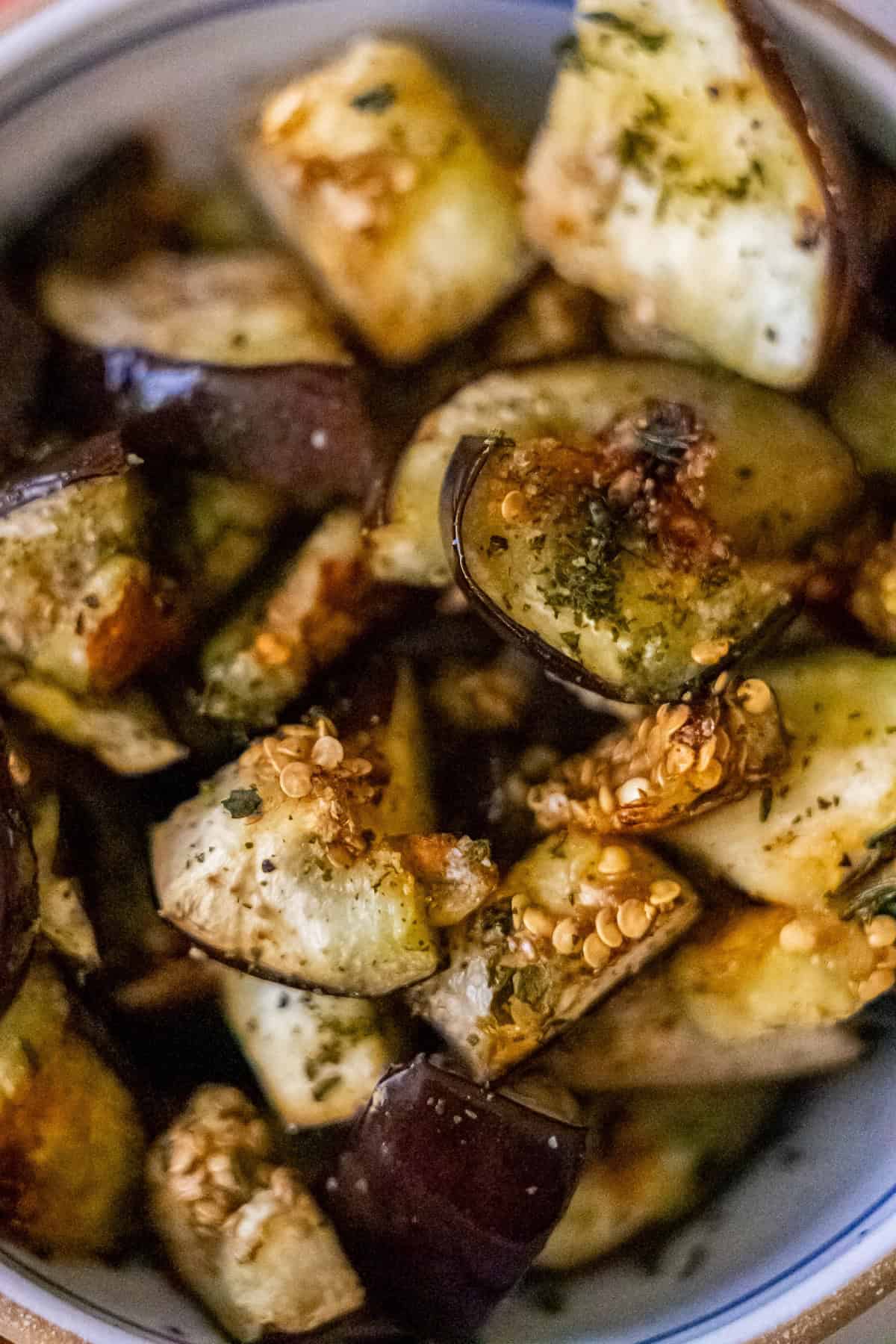 A bowl of succulent roasted eggplant pieces delicately seasoned with an aromatic blend of herbs and spices.