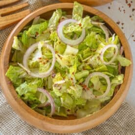 A wooden bowl filled with a fresh romaine salad, topped with sliced red onions, sprinkled with pepper, and garnished with a hint of parmesan.