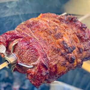 A prime rib being grilled on a rotisserie.