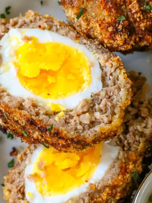 scotch eggs with keto pork rind crust cut in half on a white plate