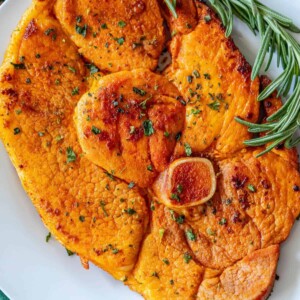 Skillet ham steak served with roasted sweet potatoes and rosemary sprigs.