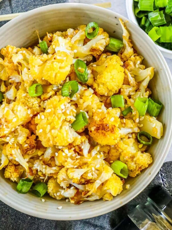 browned cauliflower with sesame seeds and chopped scallions in a white bowl on a table