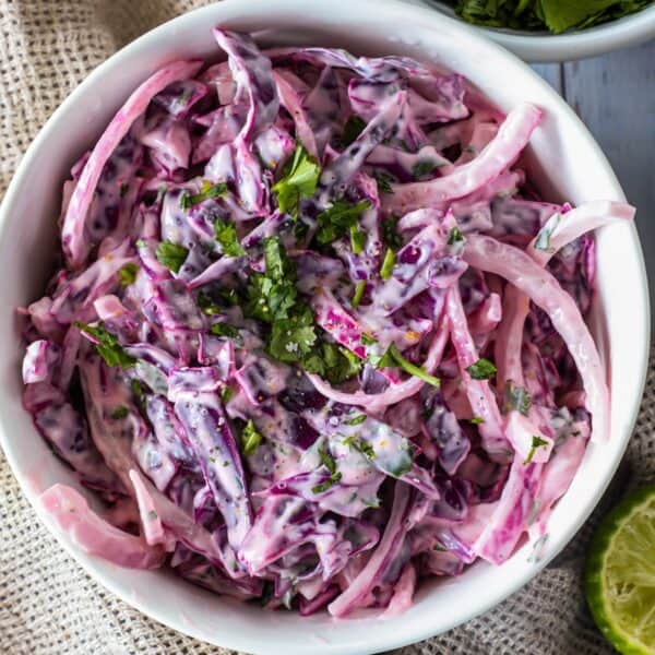 A bowl of creamy coleslaw made with purple cabbage and garnished with chopped herbs.