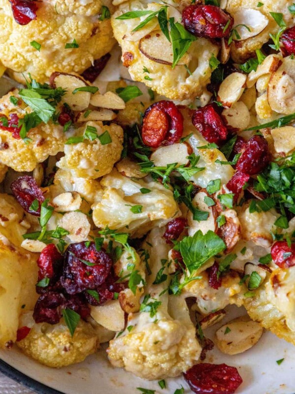 roasted cauliflower in creamy tahini sauce in a bowl with craisins, sliced almonds, and chopped parsley