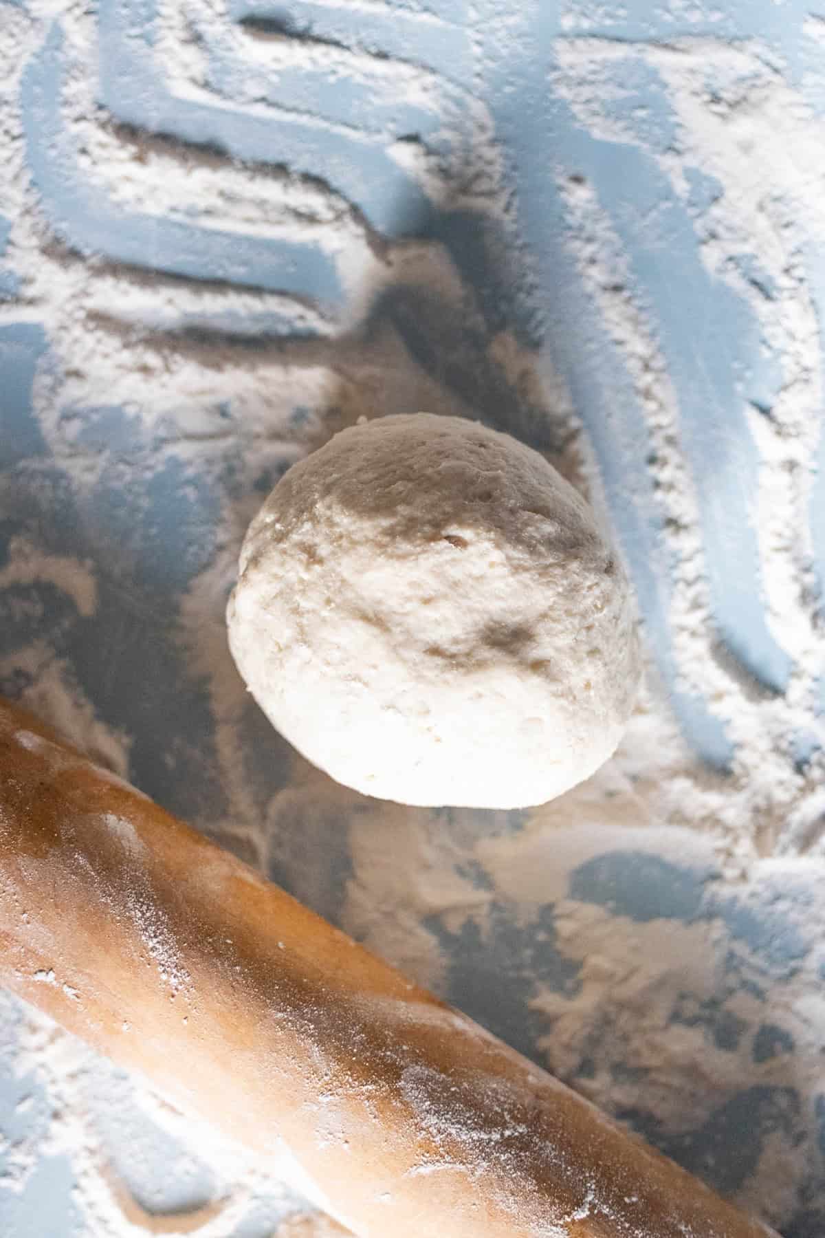 A ball of dough rests on a floured surface with a wooden rolling pin nearby, ready to be transformed into delicious Scottish Tattie Scones.