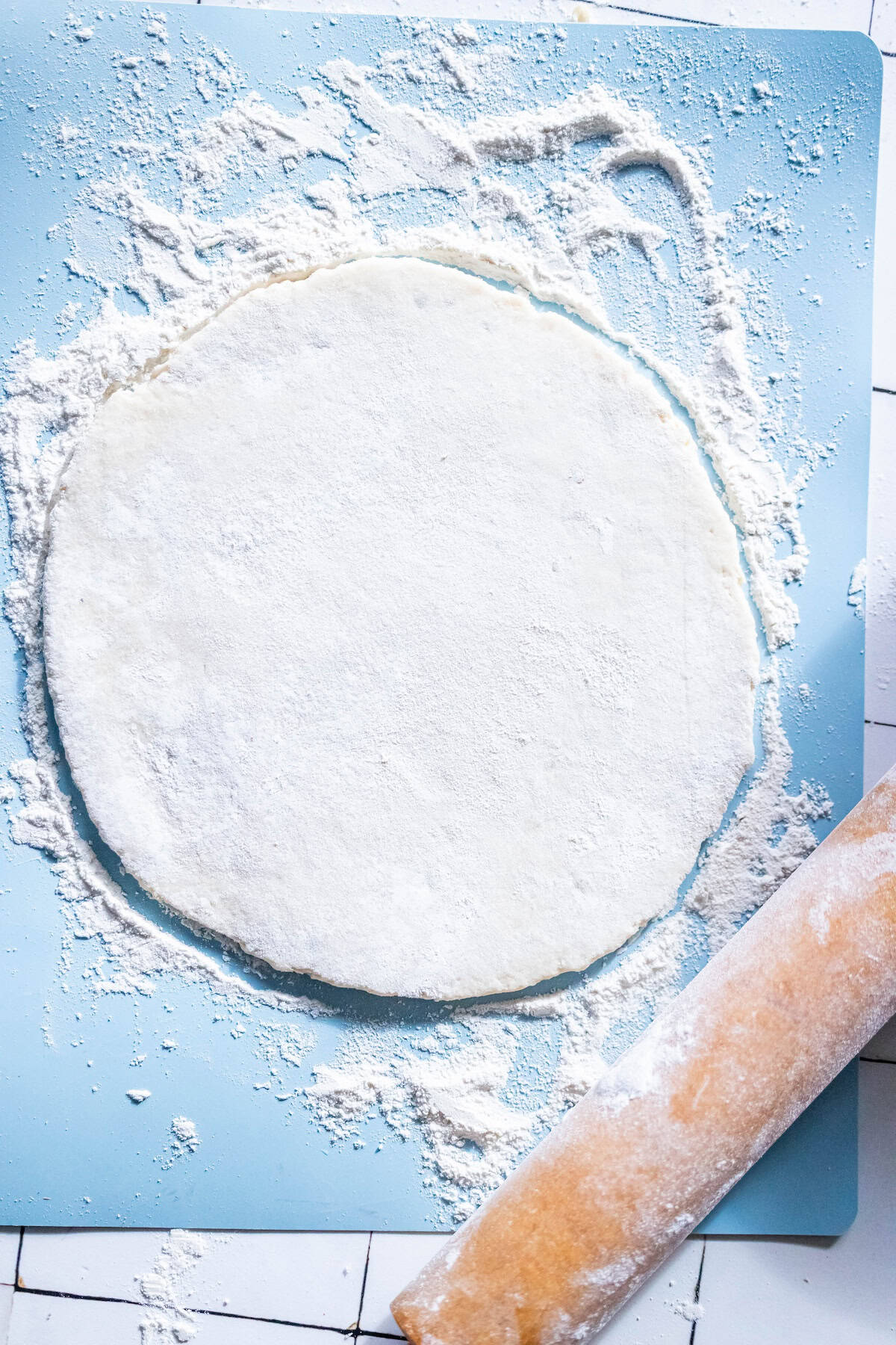 A circular sheet of dough on a floured surface, perfect for crafting authentic Scottish Tattie Scones, sits next to a well-used rolling pin.