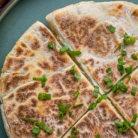 Close-up of a sliced, round Scottish flatbread topped with chopped green onions, reminiscent of traditional tattie scones.