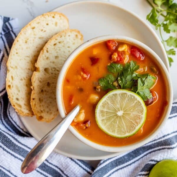 A bowl of soup with Thai chili and lime on a white plate.