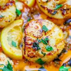 a seared scallop in a pan with chopped cilantro and chili sauce on top next to a slice of lemon