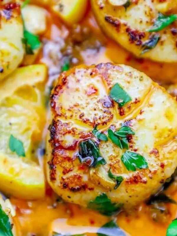 a seared scallop in a pan with chopped cilantro and chili sauce on top next to a slice of lemon