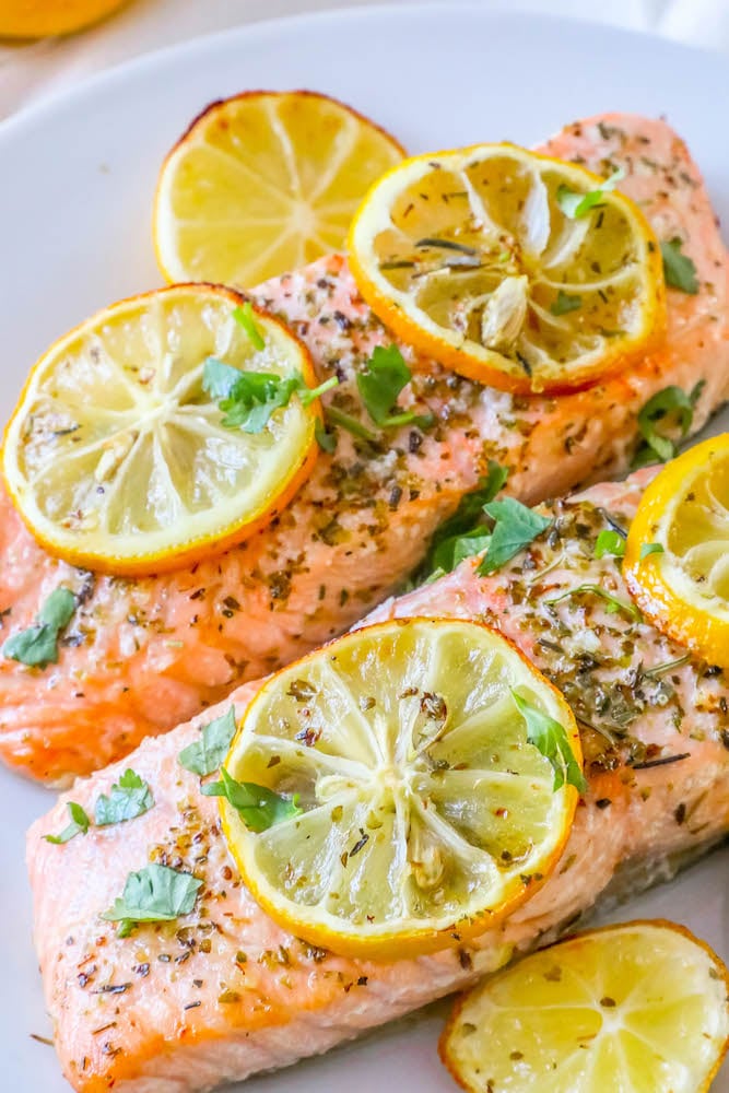 salmon filets with lemon slices, garlic and herbs on top on a white plate