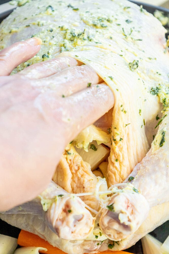 picture of a hand rubbing butter under chicken skin