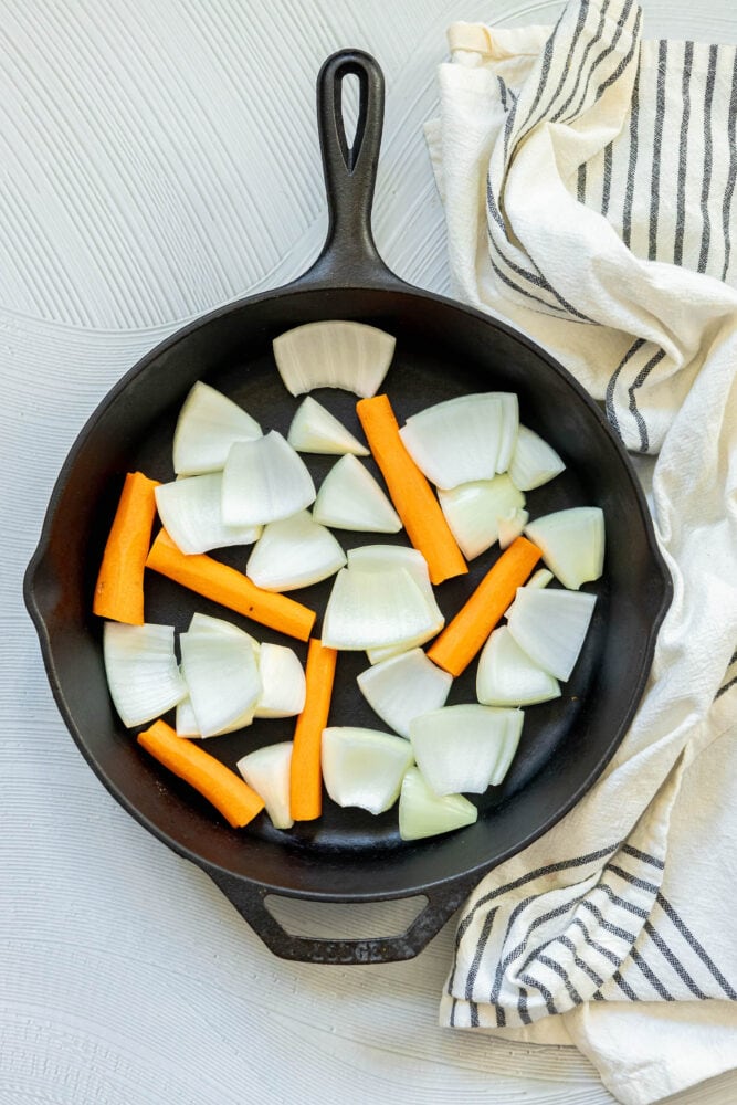 picture of a cast iron skillet with onions and carrots in the pan 