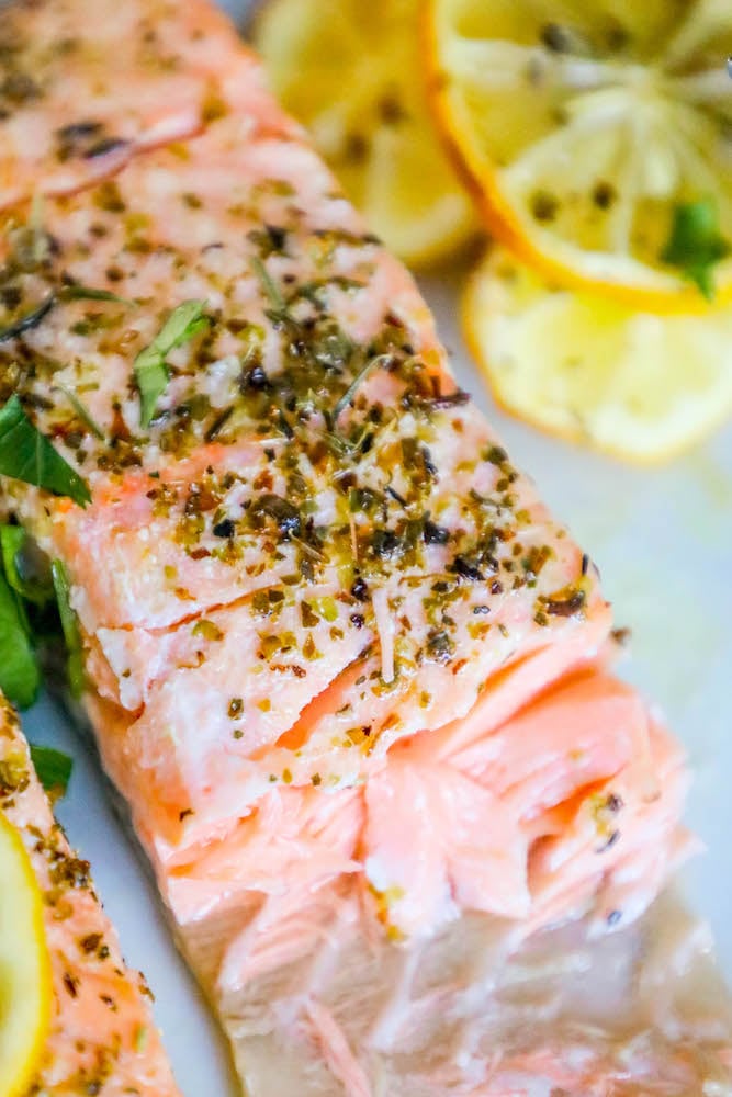 salmon filets  cut in half with lemon slices, garlic and herbs on top on a white plate