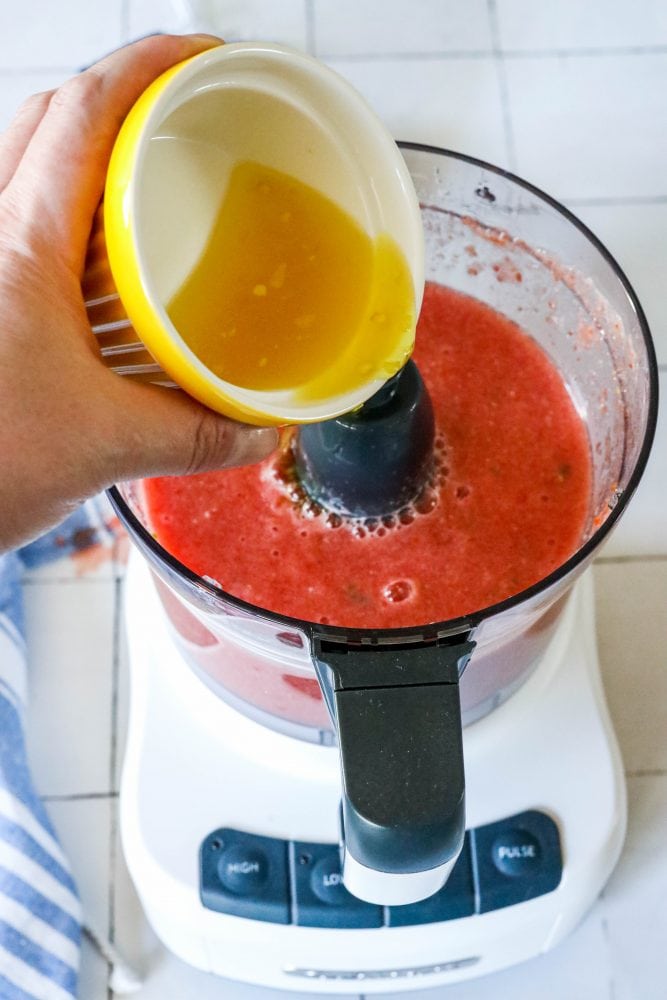 picture of a hand adding jalapeno juice to food processor with salsa in it