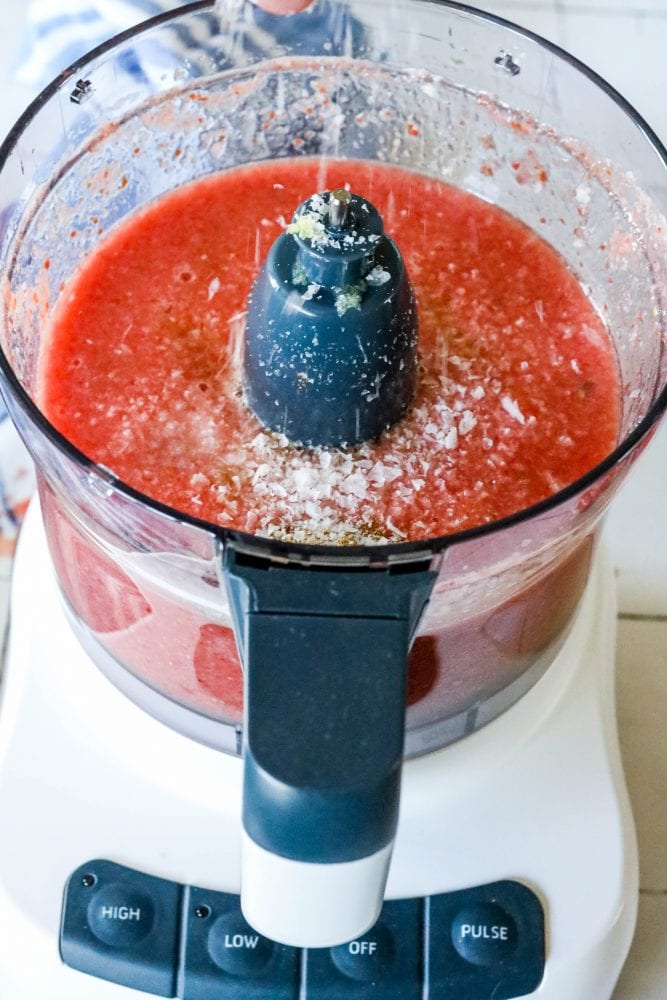 picture of hand adding salt to food processor with salsa in it