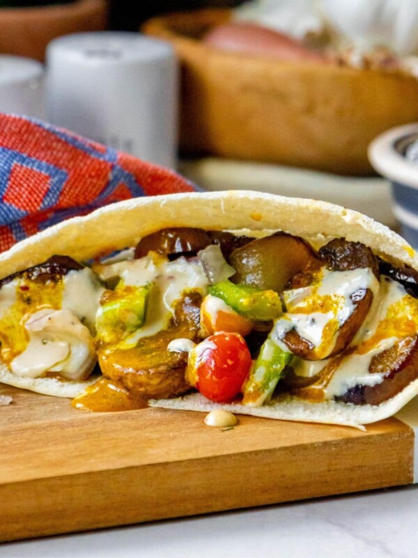 sabich sandwich with fried eggplants, fried mushrooms, Israeli salad, amba sauce, tahini sauce and hummus in a pita