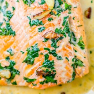 whiskey cream sauce salmon topped with chopped parsley and garlic cloves on top