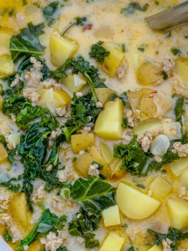 zuppa toscana soup with kale, potatoes, cream, and sausage in a white dutch oven with a ladle in it