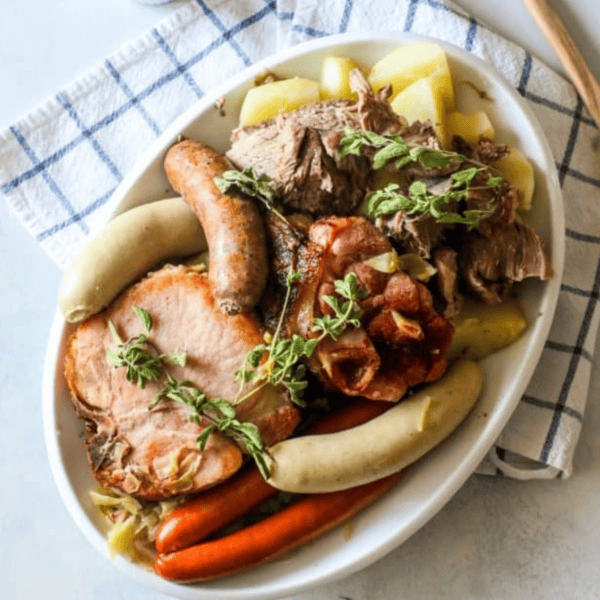 A bowl of traditional Alsace choucroute garnie with sausages, pork, potatoes, and garnished with fresh herbs.