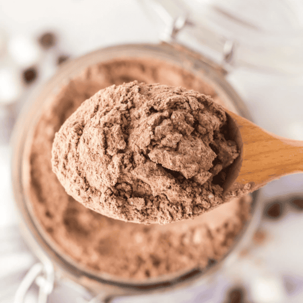 A wooden spoon scoops homemade hot cocoa mix from a jar, seen from above.