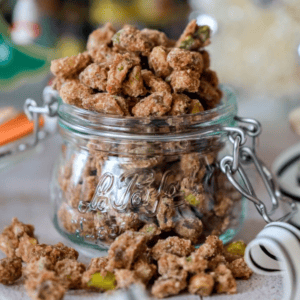 Close-up of a glass jar filled with spiced nuts. The jar is open, with some nuts spilling out onto the surface.